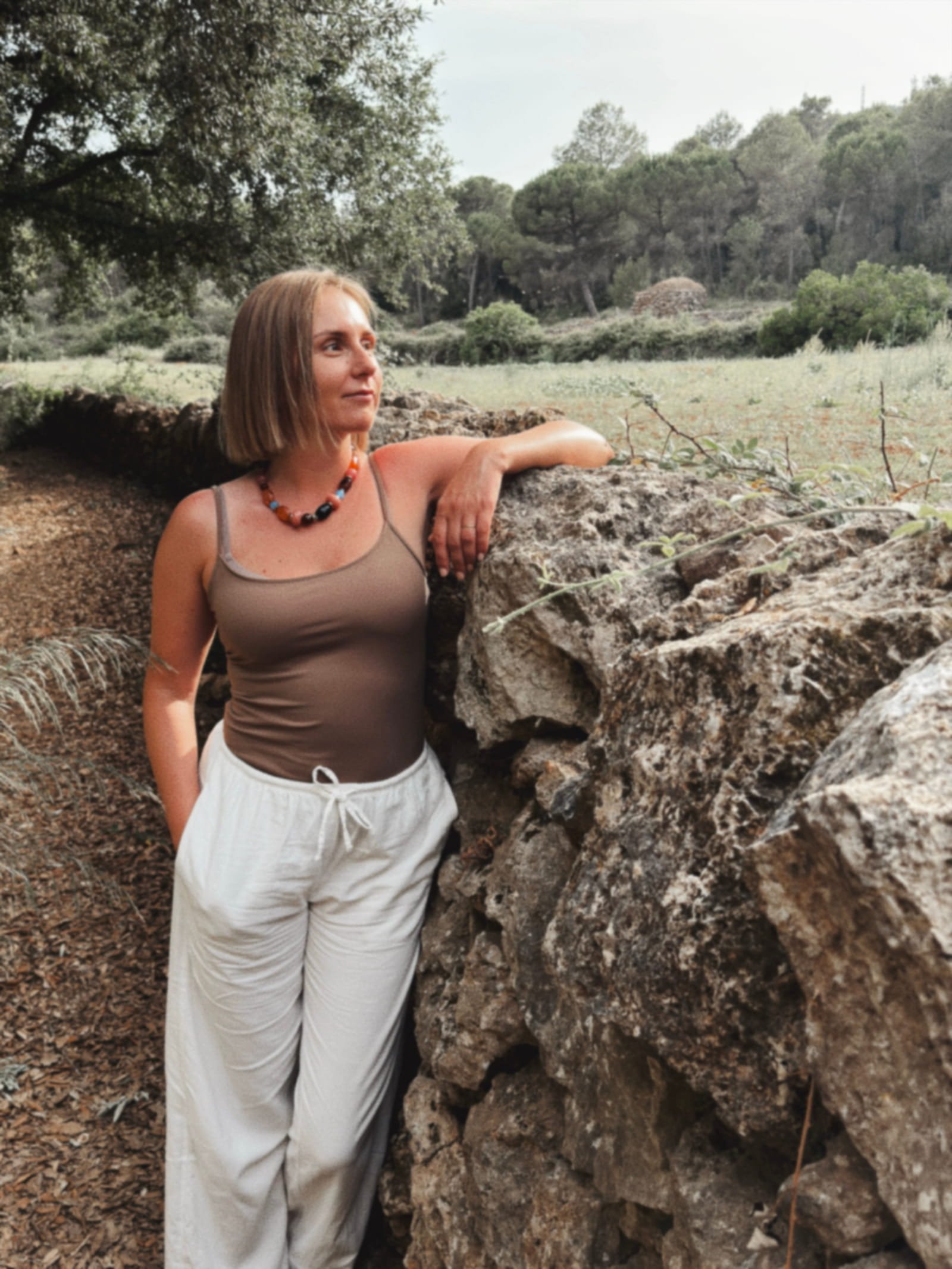 Agnie de pie junto a un muro de piedra en un entorno natural